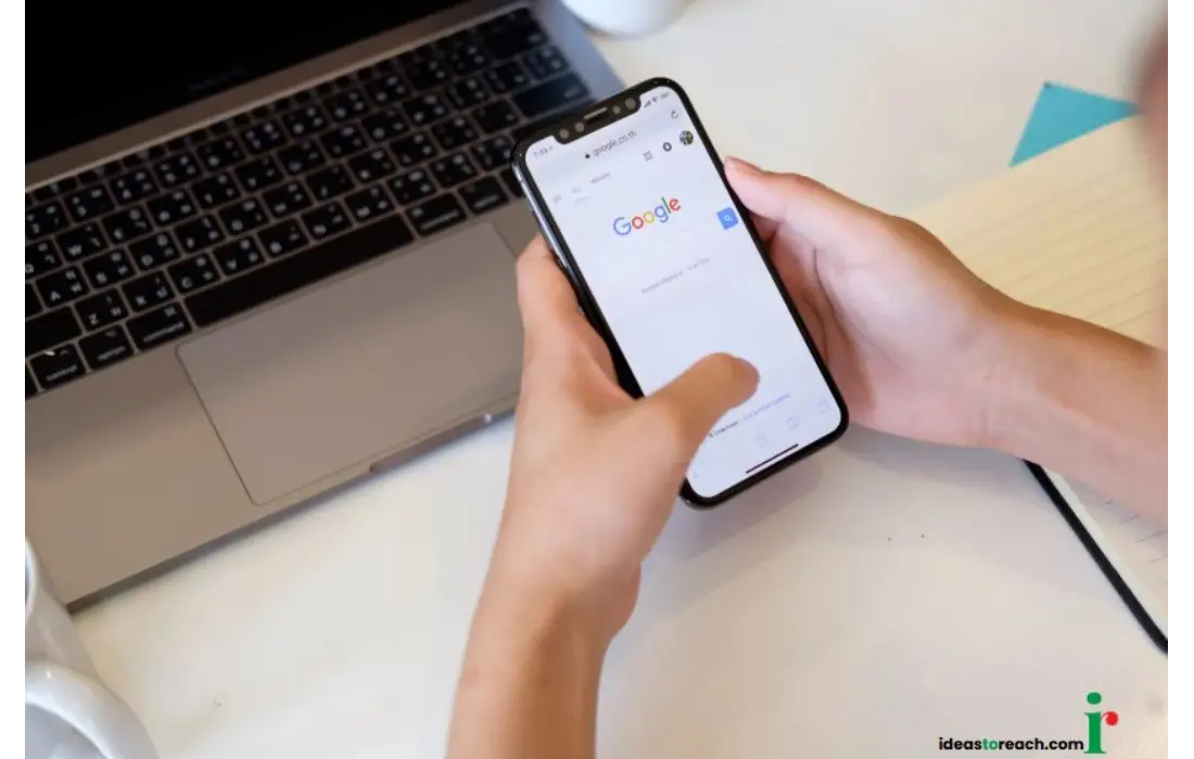 Person using Google’s new patent for personalized search from their history on a smartphone, with a laptop and notebook nearby.